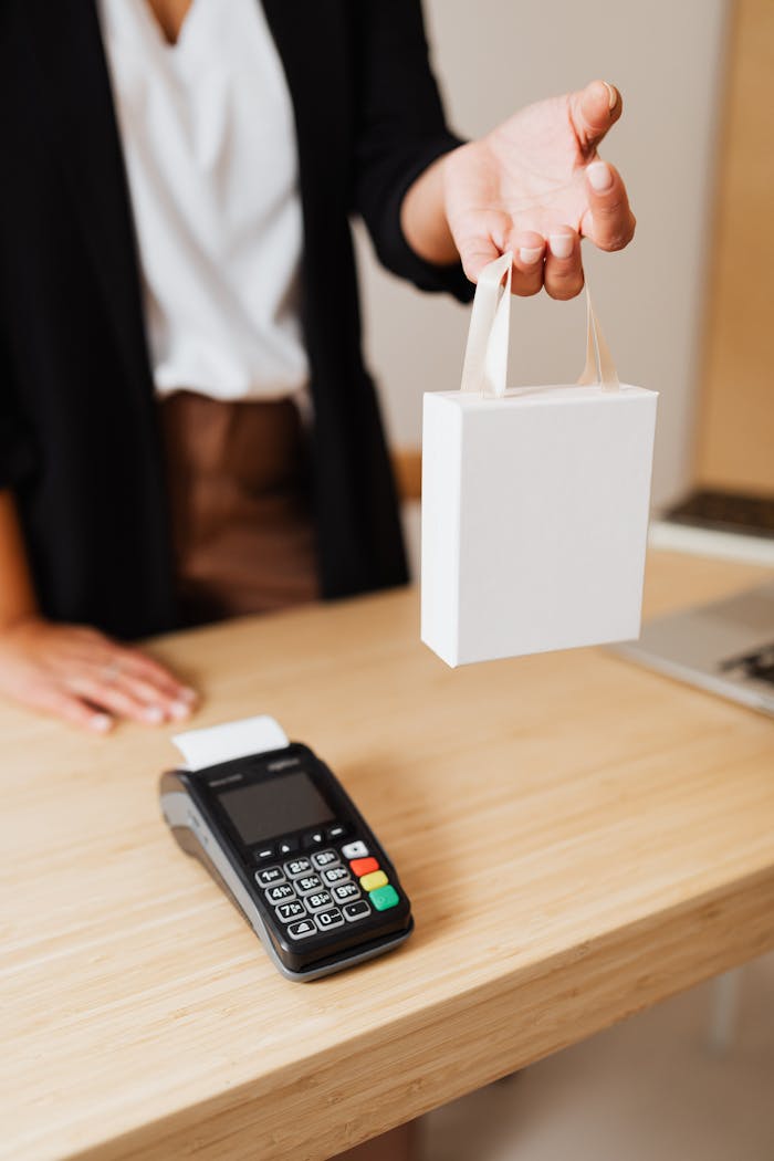 our-services-3 Close-up of shopper's hand holding a bag next to a payment terminal on a wooden counter.